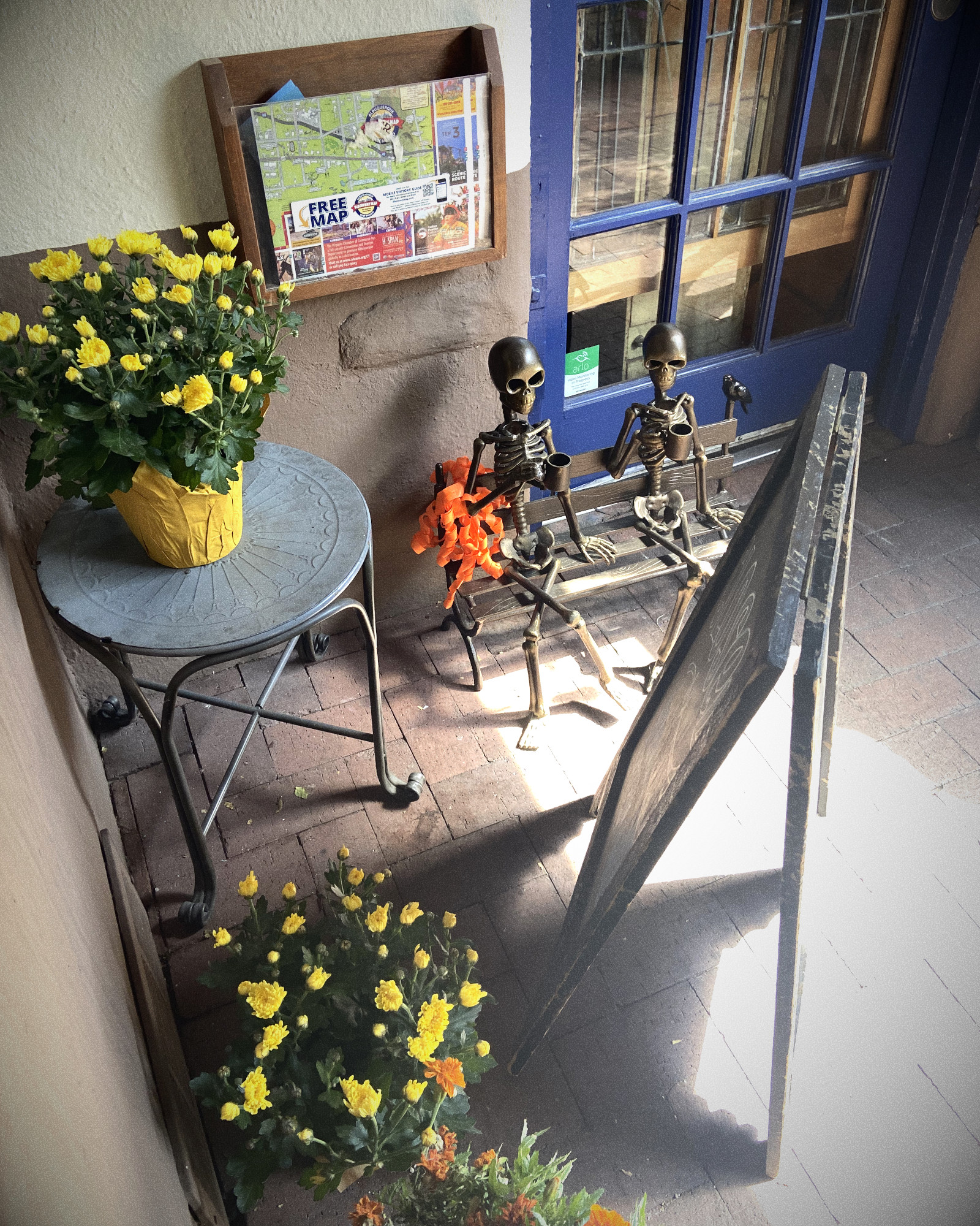 an small iron sculpture of two skeletons drinking coffee on a bench behind a cafe sign